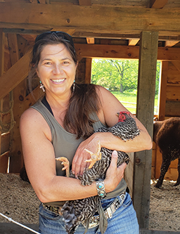 Suzanne smiling and holding a chicken in her arms